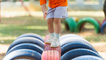 A young child is standing on a tire in a park. The tire is surrounded by other tires, creating a fun obstacle course for the child to play on. The scene is playful and lighthearted