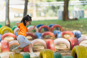 A little girl is running through a tire obstacle course. The tires are colorful and scattered...