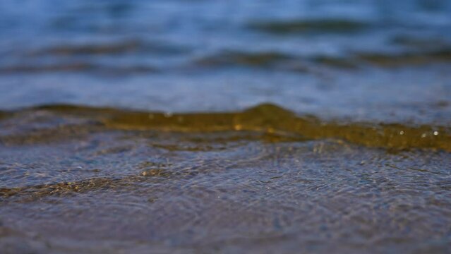Slow waves come up to the sandy shore. Close up view on the river bank on sunny day.