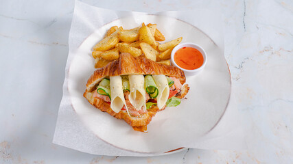 Croissant sandwich on plate with potatoes