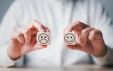 Customer service review. Hands hold smiley happy and unhappy sad emotion face on wooden cubes....