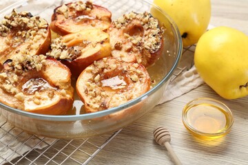 Naklejka na ściany i meble Delicious baked quinces with nuts in bowl, honey and fresh fruits on wooden table, closeup