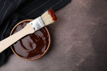 Marinade in bowl and basting brush on brown table, top view. Space for text