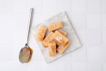 Delicious candies with sea salt and caramel sauce on white tiled table, top view