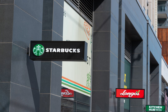 exterior projecting signs for Starbucks, a coffee shop chain, Longos, a supermarket, and Kitchen Hub, a restaurant, located at 1100 King Street West in Toronto, Canada