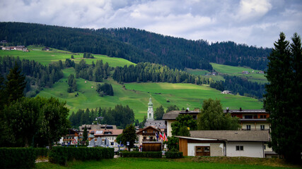 Fototapeta na wymiar Ein Dorf mit einer Kirche im Zentrum vor einem Berghang der mit Wiesen und Wald überzogen ist