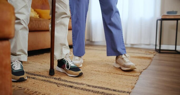 Walking stick, help and feet of nurse with senior patient in a nursing home with support, guidance or healing closeup. Balance, cane and legs or caregiver holding elderly patient with a disability