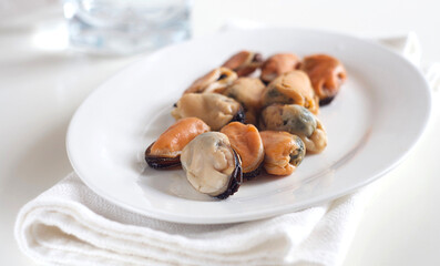 Mussels lie in a white plate on a white table