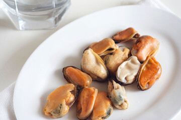Mussels lie in a white plate on a white table 