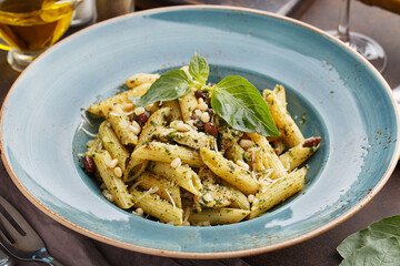 Pasta penne with chicken, pine nuts, beans, pesto sauce and basil leaves on dark concrete background. Side view, close up, selective focus