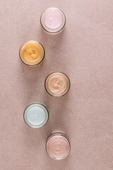 Set of cosmetic cream of various colors in glass jars on beige stone background. Top Vertical view. of the space. Layout for product advertising