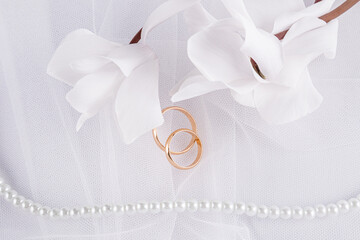 Fototapeta na wymiar Delicate wedding arrangement with two wedding gold rings on a white veil background with pearl beads and flowers. postcard. invitation. cover