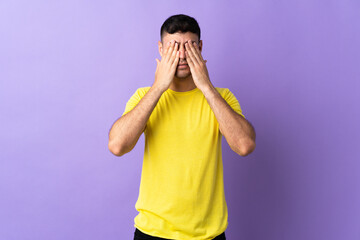 Young Colombian man isolated on purple background covering eyes by hands