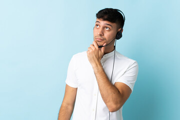 Telemarketer Colombian man working with a headset over isolated background having doubts and...