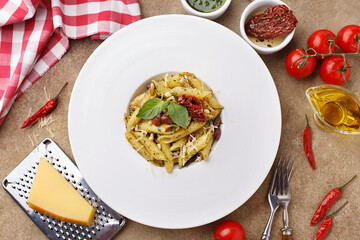 Italian pasta penne with sun dried tomatoes, pine nuts, beans, pesto sauce and basil leaves on beige concrete background. Top view