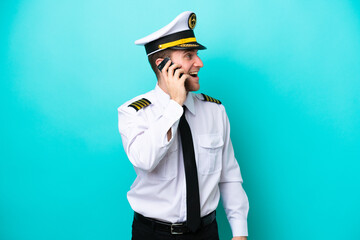 Airplane caucasian pilot isolated on blue background keeping a conversation with the mobile phone © luismolinero