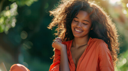 A woman in an orange dress smiles as sunlight highlights her flowing hair.