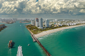 Fototapeta premium Commercial container ship entering Miami port harbor through main channel near South Beach. Luxurious hotels and residential buildings on waterfront and high skyscraper towers of downtown in distance