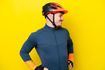 Young cyclist caucasian man isolated on yellow background suffering from backache for having made an effort