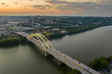 Naklejka premium Highway traffic with driving cars on bridge in downtown district of Cincinnati city in Ohio, USA. American city skyline with brightly illuminated high commercial buildings at sunset