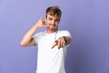 Young handsome blonde man isolated on purple background making phone gesture and pointing front