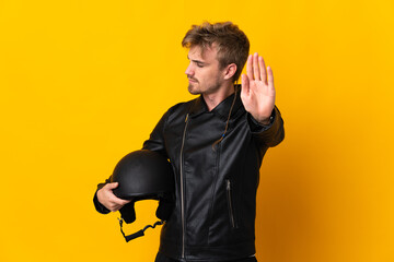 Man with a motorcycle helmet isolated on yellow background making stop gesture and disappointed