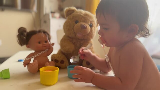 girl plays with plush toys. happy family child dream concept. baby girl with a pacifier in her mouth feeds from a spoon, plush toy bear and doll. child lifestyle playing with toys