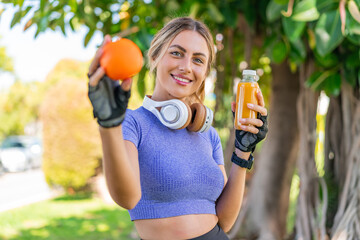 Young pretty sport woman at outdoors holding an orange and an orange juice