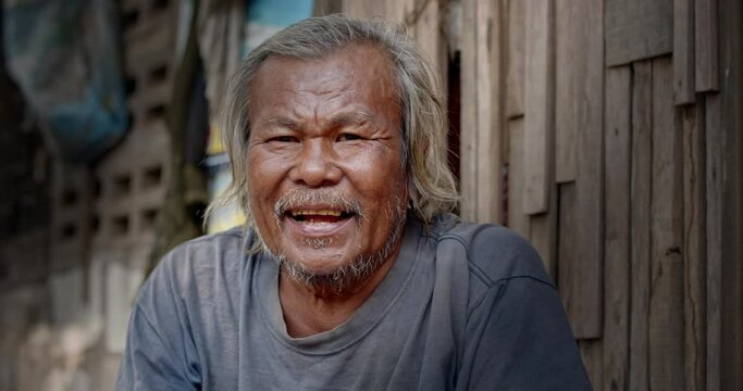 A smiling Asian man who is a homeless ragpicker or has a career collecting garbage and selling it, live in a abandoned house at a slum village.
