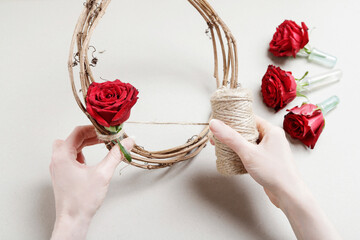 Florist at work: woman shows how to make a Christmas door wreath with roses, fir and cinnamon...