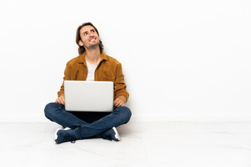Young man with his laptop sitting one the floor looking up while smiling