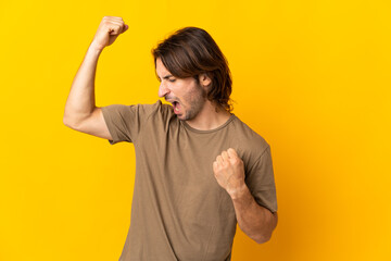 Young handsome man isolated on yellow background celebrating a victory