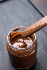 chocolate sauce in a glass jar on a brown background, closeup