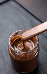 chocolate sauce in a glass jar on a brown background, closeup