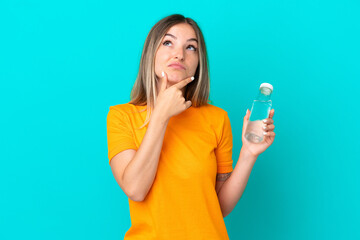 Young Romanian woman with a bottle of water isolated on blue background having doubts