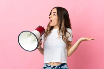 Foto op Plexiglas Young Romanian woman isolated on pink background holding a megaphone and with surprise facial expression © luismolinero