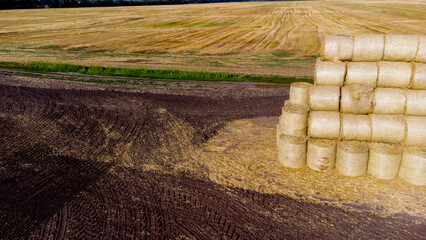 Many bales and rolls of straw after the harvest collected together on field on sunny autumn summer day. Agricultural agro-industrial agrarian landscape. Agribusiness agro business. Aerial drone view.