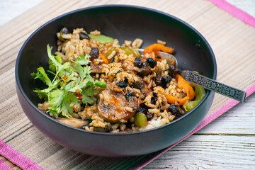 Vegan rice and mushroom pilaf, black bowl, wooden mat and table.. Chinese cuisine