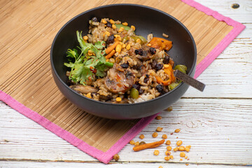 Vegan rice and mushroom pilaf, black bowl, wooden mat and table.. Chinese cuisine