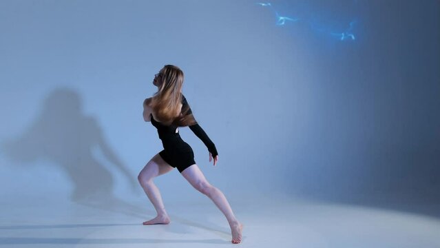 A beautiful girl with long flowing hair makes a pirouette in the studio. Slow motion.