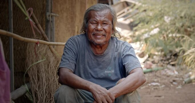 A smiling Asian man who is a homeless ragpicker or has a career collecting garbage and selling it, live in a abandoned house at a slum village.