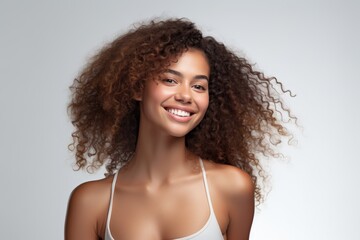Gorgeous woman with voluminous curly hair and a beaming smile, wearing a white tank top