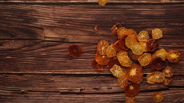 A stack of dehydrated oranges sits on a rustic wooden table with a brown wood stain. The hardwood plank flooring complements the natural plant pattern, enhanced by a glossy varnish finish