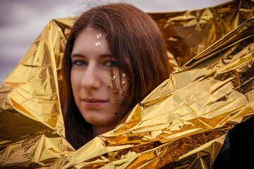 woman as a fantasy representation with tacks in her face and a golden rescue blanket