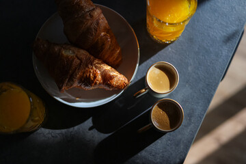 Coffee, croissants and orange juice on a dark stone table. Breakfast in the morning sun light.