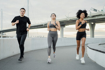 Three people jogging together on an urban bridge path, diverse and fit, city skyline in the...