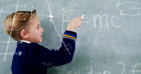 Image of math formulas over caucasian boy writing on blackboard