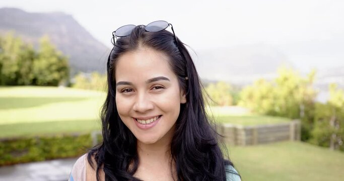 A young biracial woman smiles outdoors, greenery in the background