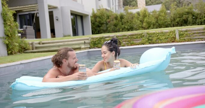 A young Caucasian couple relaxes in a pool with drinks