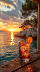 A glass with an orange cocktail and a slice of orange near the water against the backdrop of sunset over the sea.
Concept: summer vacation, advertising of resorts and spas, restaurant menu of alcohol 